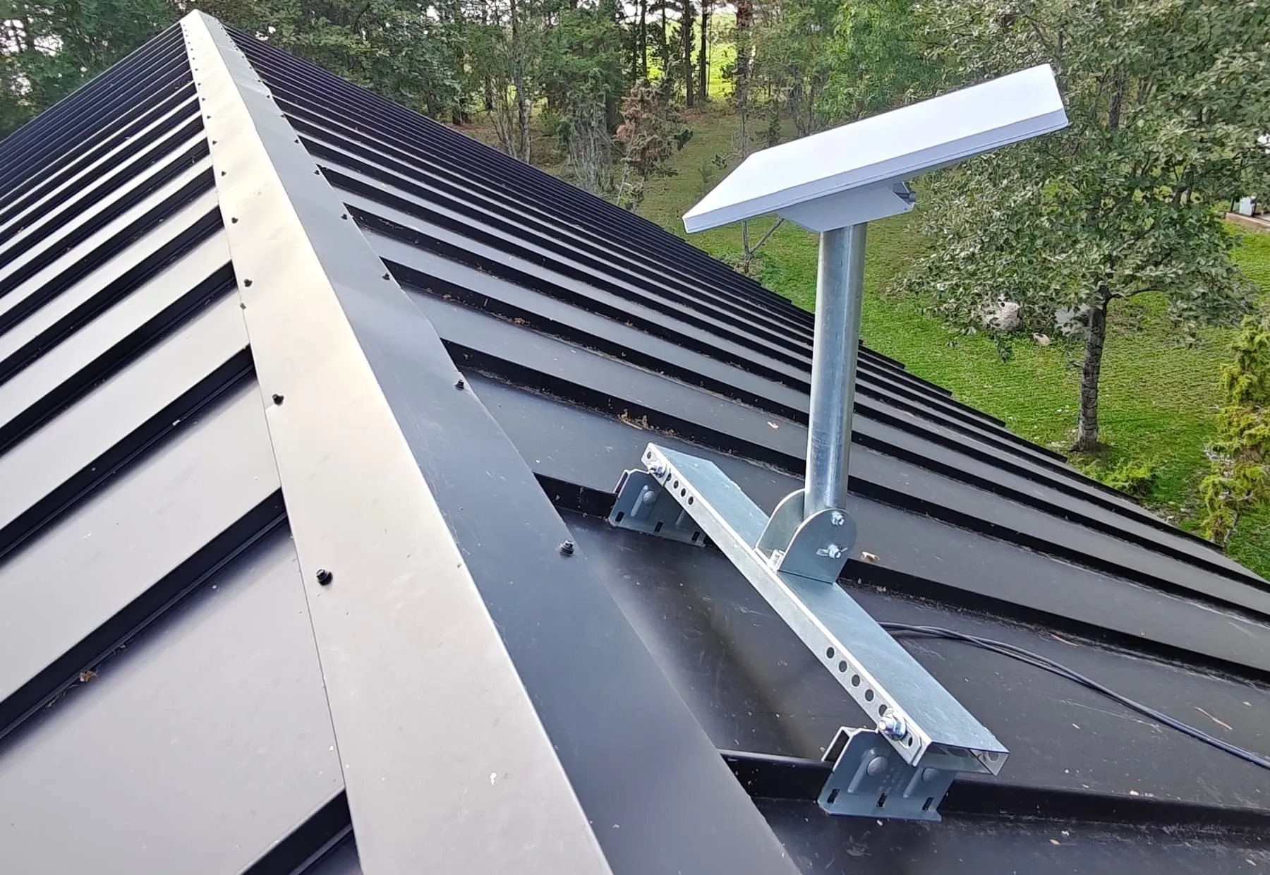 A Starlink dish on a galvanised FalsMount mount clamped to the seams of a dark standing-seam metal roof